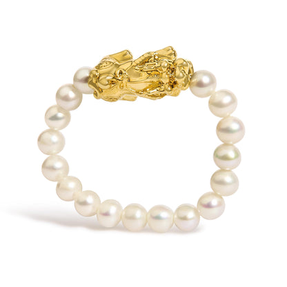 Close-up front angle of a yellow metal ring with detailed sculptural design, surrounded by a string of white round pearls, shown against a white background.