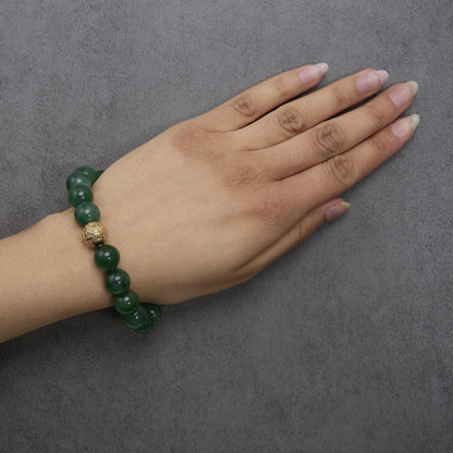 Yellow metal bracelet with round green gemstone beads and a decorative yellow metal bead, worn on a model's wrist, top-down angle.