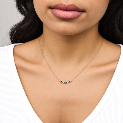 Close-up front view of a model wearing a yellow metal necklace with alternating marquise-shaped green gemstones and round white gemstones in bezel settings.