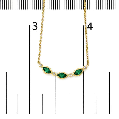 Yellow necklace with green marquise-shaped gemstones and white round gemstones in bezel settings, shown on a scale, top-down angle.