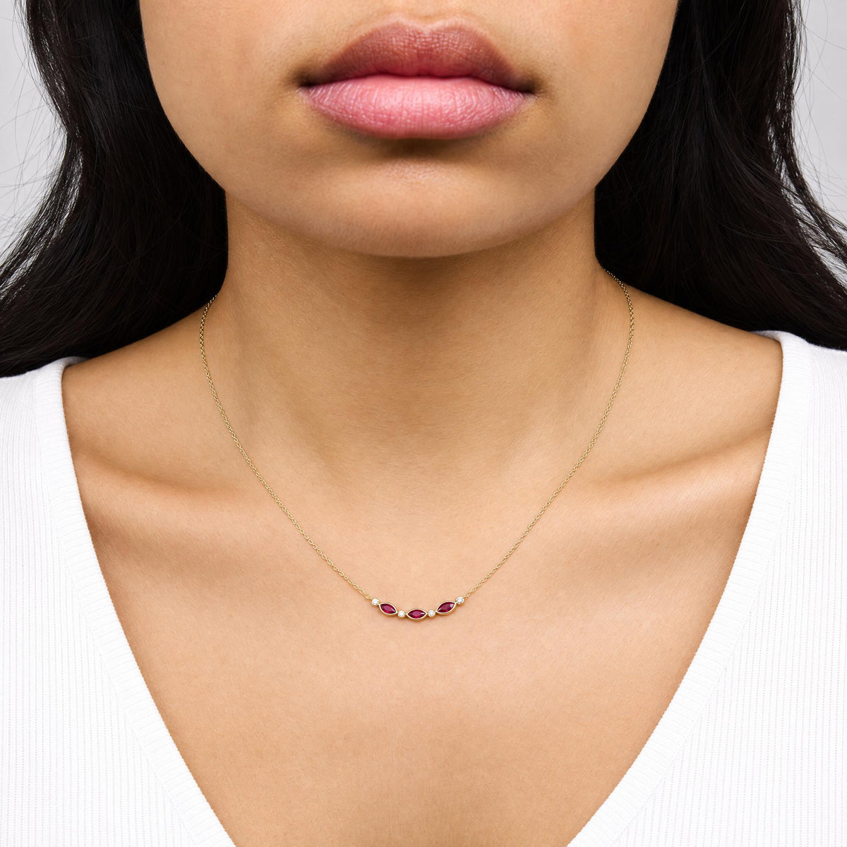 Close-up front view of a model wearing a yellow necklace with a curved pendant featuring marquise-shaped red gemstones and round white gemstones in bezel and prong settings.