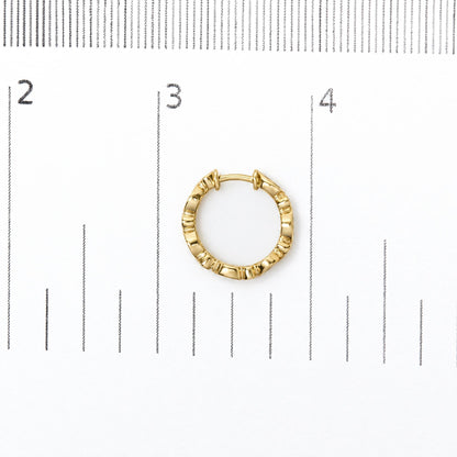 Close-up front view of a single yellow metal hoop earring with textured ridges, placed on a measurement scale.