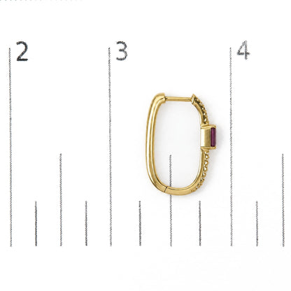 Close-up front angle of a single yellow metal earring shown on a scale, oval-shaped hoop design with small round white gemstones in prong settings along one side and a red rectangular gemstone set in prongs near the clasp.