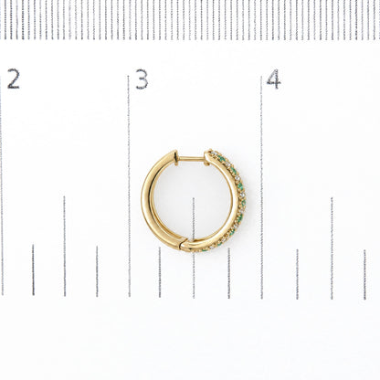 Close-up front view of a yellow metal hoop earring shown on a ruler scale, featuring alternating round white and green gemstones in prong settings along the outer edge.
