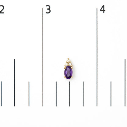 Close-up front view of a single yellow metal earring displayed on a scale, featuring an oval-shaped purple gemstone below a cluster of round white gemstones in prong settings.