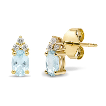 Close-up front and side view of yellow metal earrings featuring oval blue gemstones held by prongs, topped with clusters of round white gemstones in prong settings.