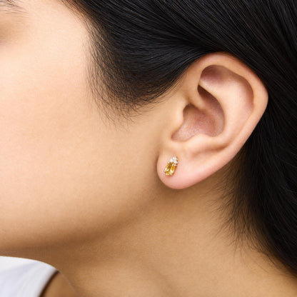 Close-up side view of a model wearing yellow metal earrings featuring oval yellow gemstones and round white gemstones in prong settings.