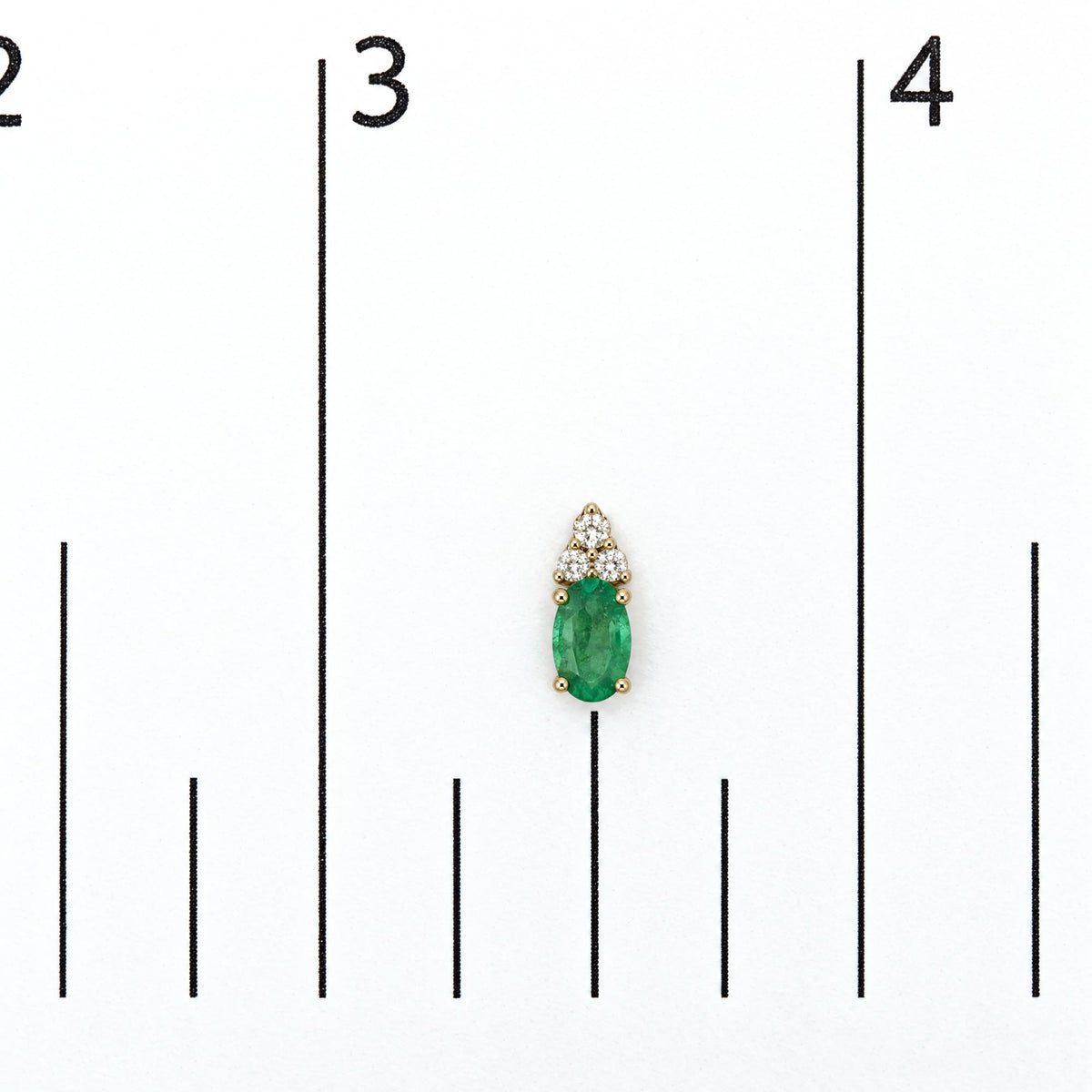 Close-up front view of yellow metal earrings shown on a scale, featuring oval green gemstones with surrounding round white gemstones in prong settings.