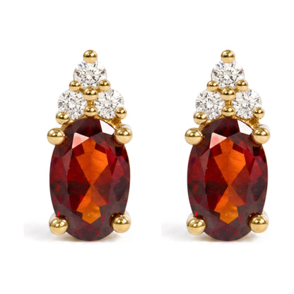 Close-up front angle of a pair of yellow metal earrings featuring an oval red gemstone in prong setting surrounded by round white gemstones in prong settings.