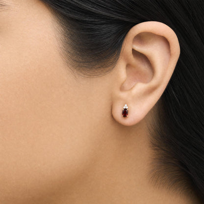 Close-up side view of a model wearing yellow metal earrings featuring an oval red gemstone with three small round white gemstones above it in a prong setting.