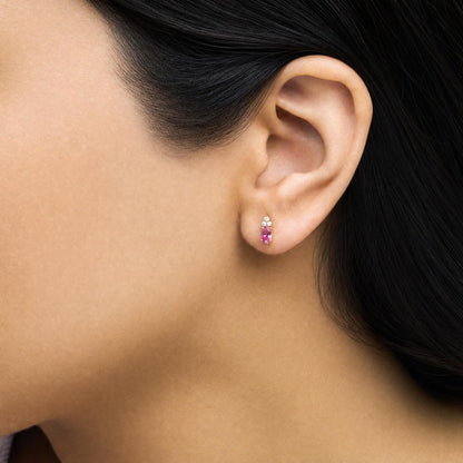 Close-up side view of a model wearing yellow metal earrings featuring an oval pink gemstone set below a cluster of round white gemstones in prong settings.