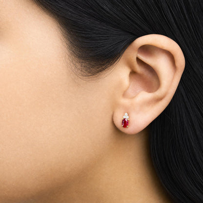Close-up side view of a model wearing yellow metal earrings featuring oval red gemstones with prong settings, accented by round white gemstones with prong settings above.