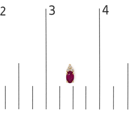 Pair of yellow earrings shown on a scale, each featuring an oval red gemstone at the center topped with a triangular cluster of round white gemstones, all set in prongs. Shot is a close-up from the front.