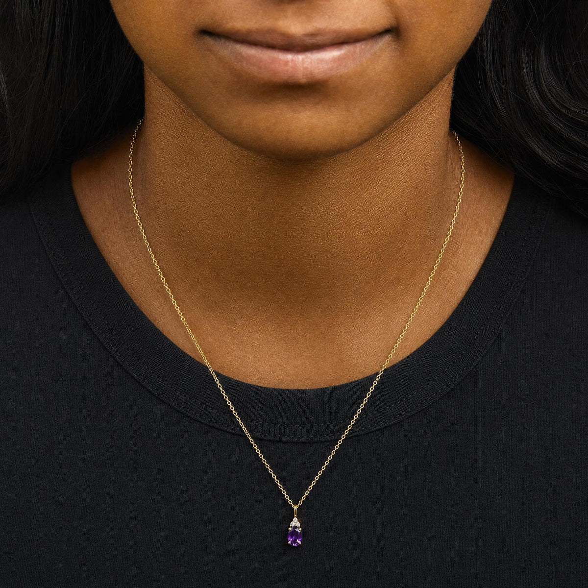 Yellow metal necklace with a pear-shaped purple gemstone and three round white gemstones above it, shown worn on a model from a front angle.