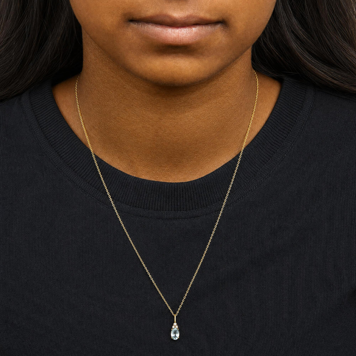 Yellow necklace with a pendant featuring an oval blue gemstone surrounded by three small round white gemstones in prong settings, shown worn on a model from the front.