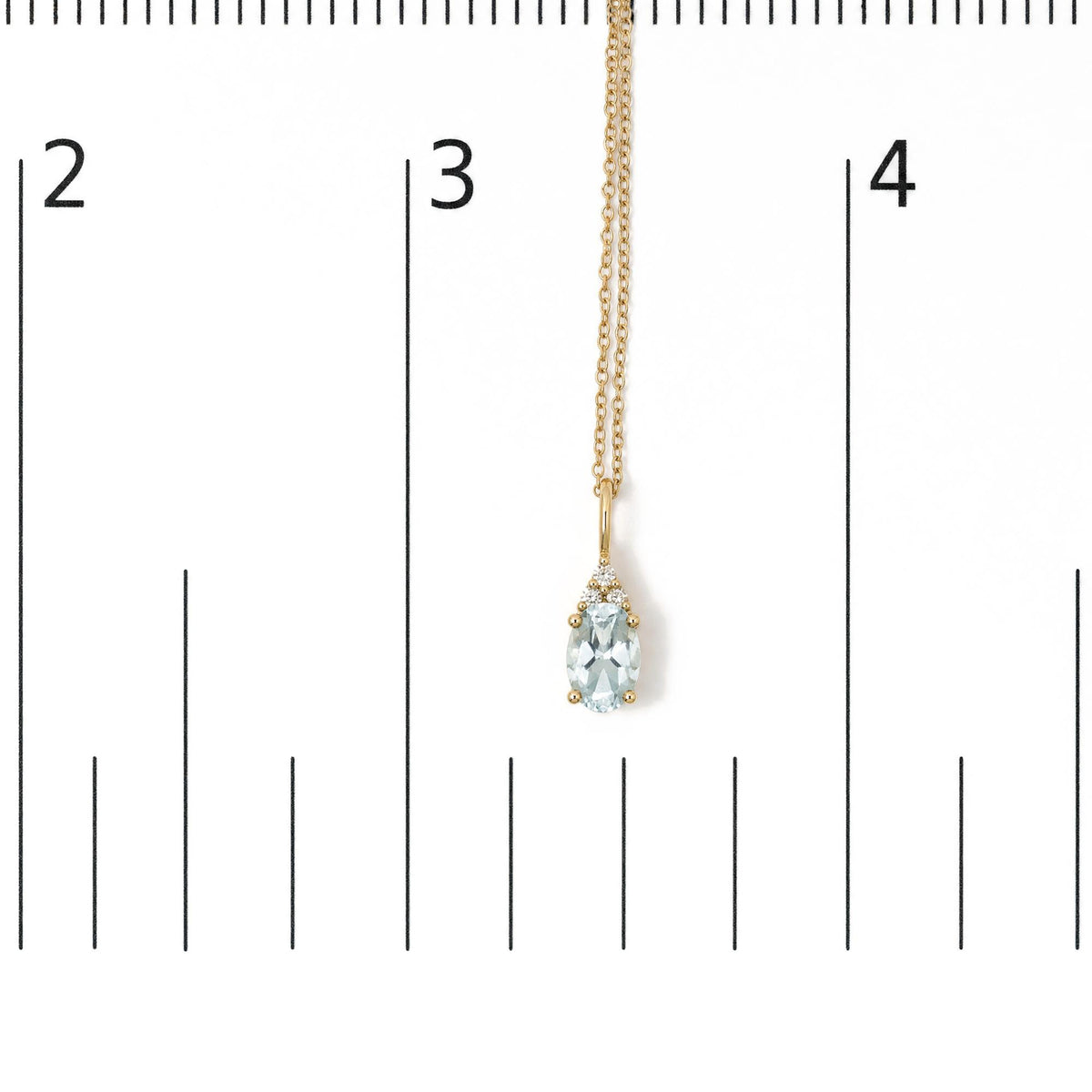 Close-up front view of a yellow metal necklace shown on a scale, featuring an oval blue gemstone pendant accented with round white gemstones in prong settings. The necklace is hanging straight down.
