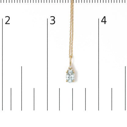 Close-up front view of a yellow metal necklace shown on a scale, featuring an oval blue gemstone pendant accented with round white gemstones in prong settings. The necklace is hanging straight down.