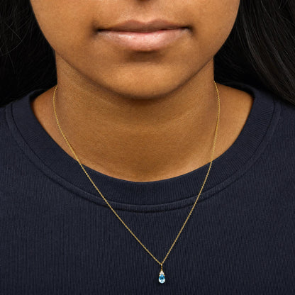 Close-up front view of a model wearing a yellow metal necklace with a pendant featuring a blue oval gemstone and three small white round gemstones set above it.