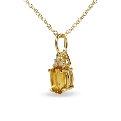 Close-up front view of a yellow metal necklace pendant with an oval yellow gemstone in a prong setting, accented by three round white gemstones in prong settings, shown hanging from a yellow metal chain.