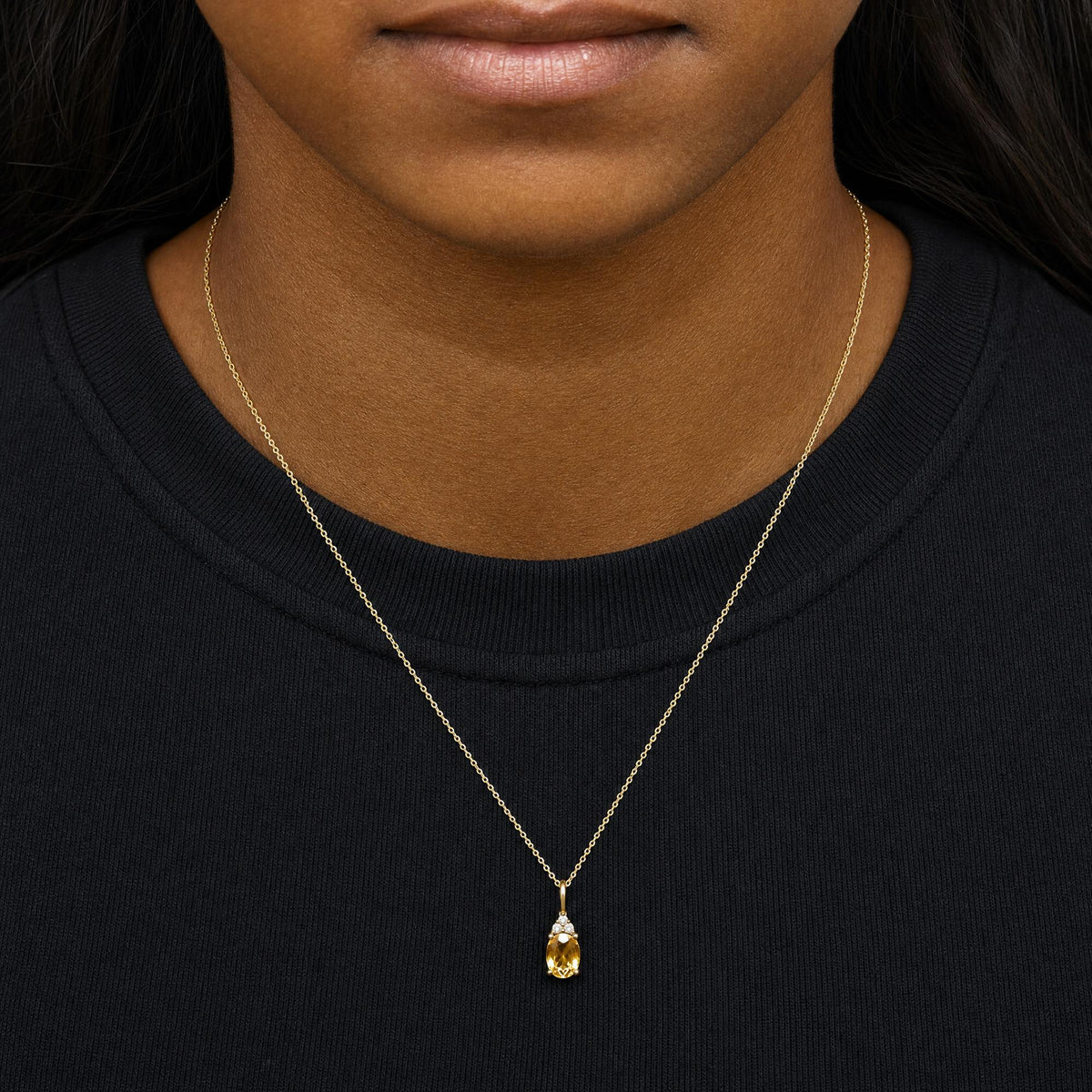 Yellow metal necklace with oval yellow gemstone pendant and three small round white gemstones above, shown worn on model from a front close-up angle.