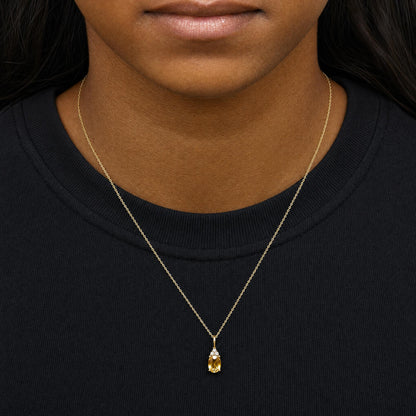 Yellow metal necklace with oval yellow gemstone pendant and three small round white gemstones above, shown worn on model from a front close-up angle.