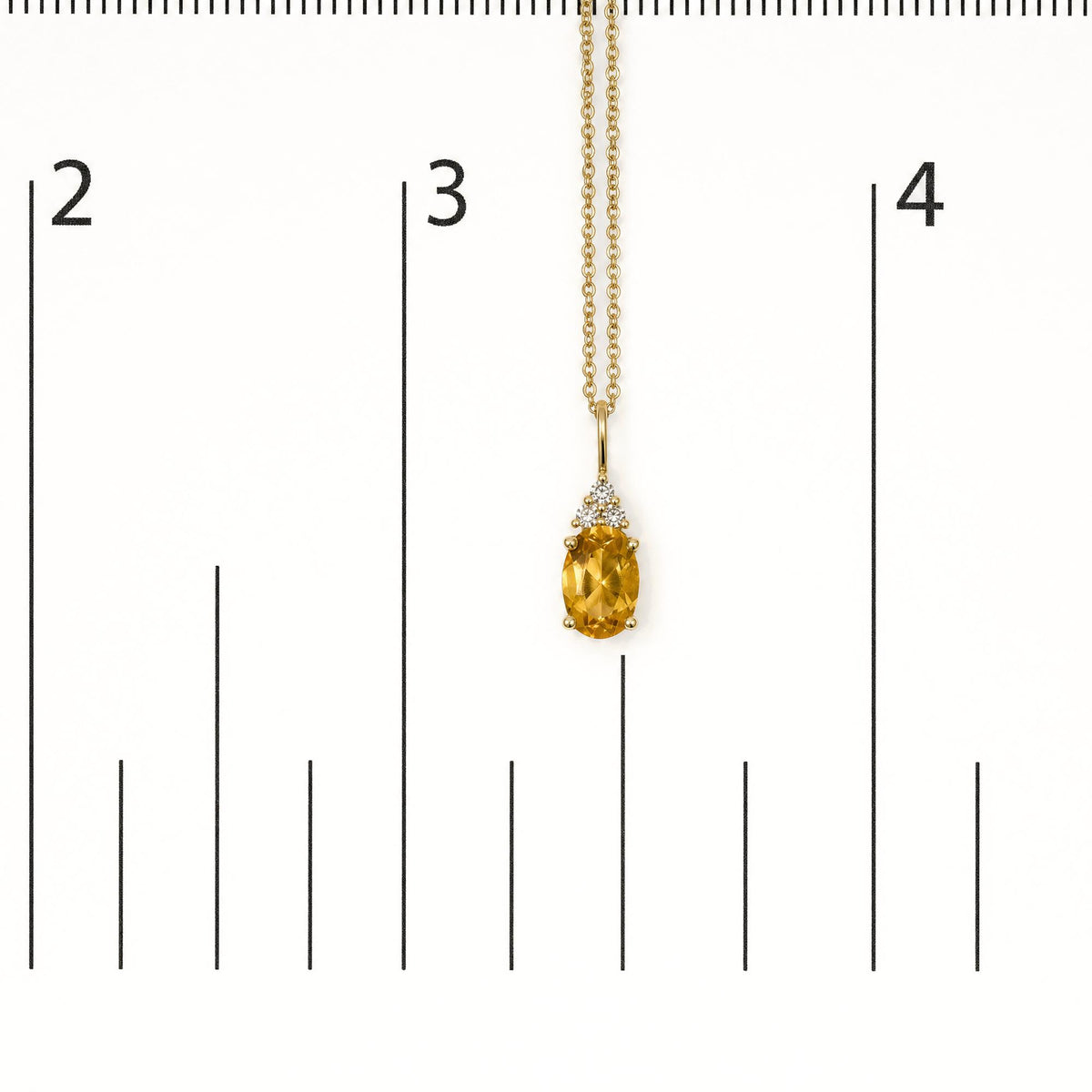 Yellow metal necklace with a pendant featuring an oval yellow gemstone set in prongs, accented by three round white gemstones above it, shown on a measurement scale from a front angle.