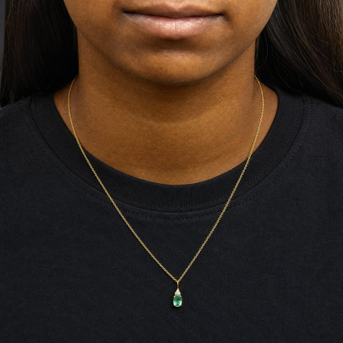 Yellow necklace with a pendant featuring an oval green gemstone and three small round white gemstones above it, worn by a model, front view.