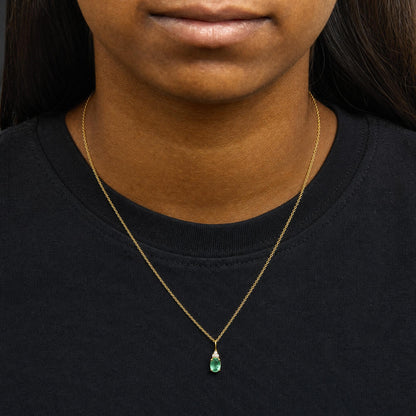 Yellow necklace with a pendant featuring an oval green gemstone and three small round white gemstones above it, worn by a model, front view.