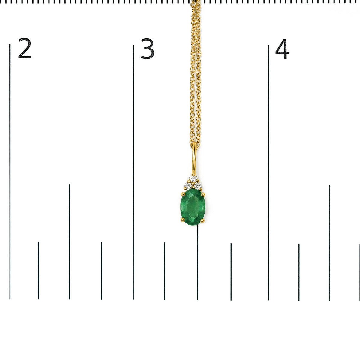 Yellow metal necklace with an oval green gemstone pendant accented by three round white gemstones in prong settings, shown on a scale, front angle.