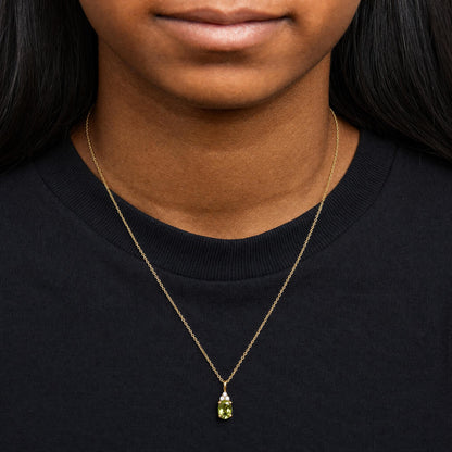 Close-up front view of a model wearing a yellow metal necklace with a pendant featuring an oval green gemstone and three round white gemstones above it.