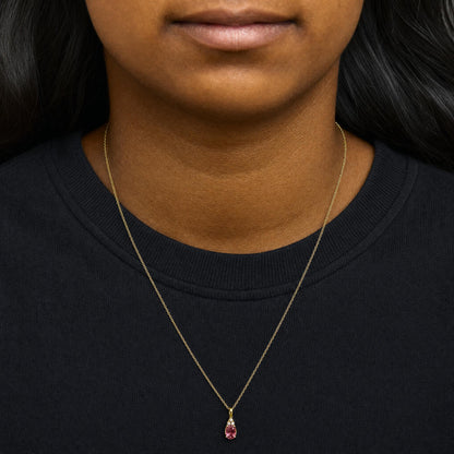 Close-up front view of a model wearing a yellow metal necklace with an oval pink gemstone pendant accented by three small round white gemstones above it.
