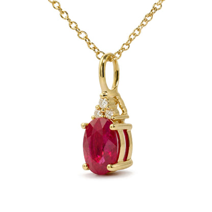Close-up front angle of a yellow metal necklace pendant featuring a red oval gemstone prong set with three round white gemstones above it in a triangular arrangement.