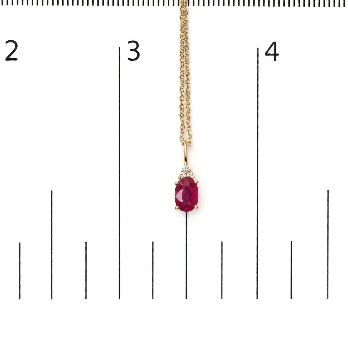 Yellow necklace with an oval red gemstone pendant surrounded by three small round white gemstones in a prong setting, shown on a scale with a front view.