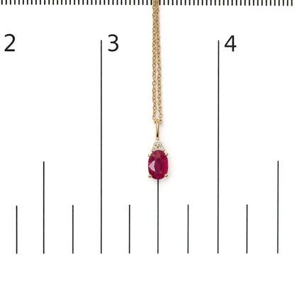 Yellow necklace with an oval red gemstone pendant surrounded by three small round white gemstones in a prong setting, shown on a scale with a front view.