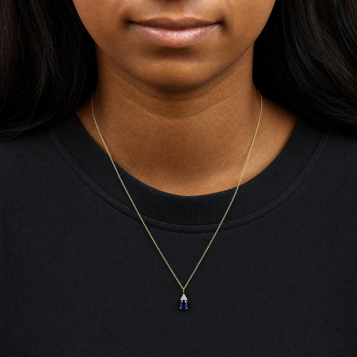 Yellow necklace with an oval blue gemstone pendant accented by three round white gemstones, shown worn on a model in a front-facing close-up shot.
