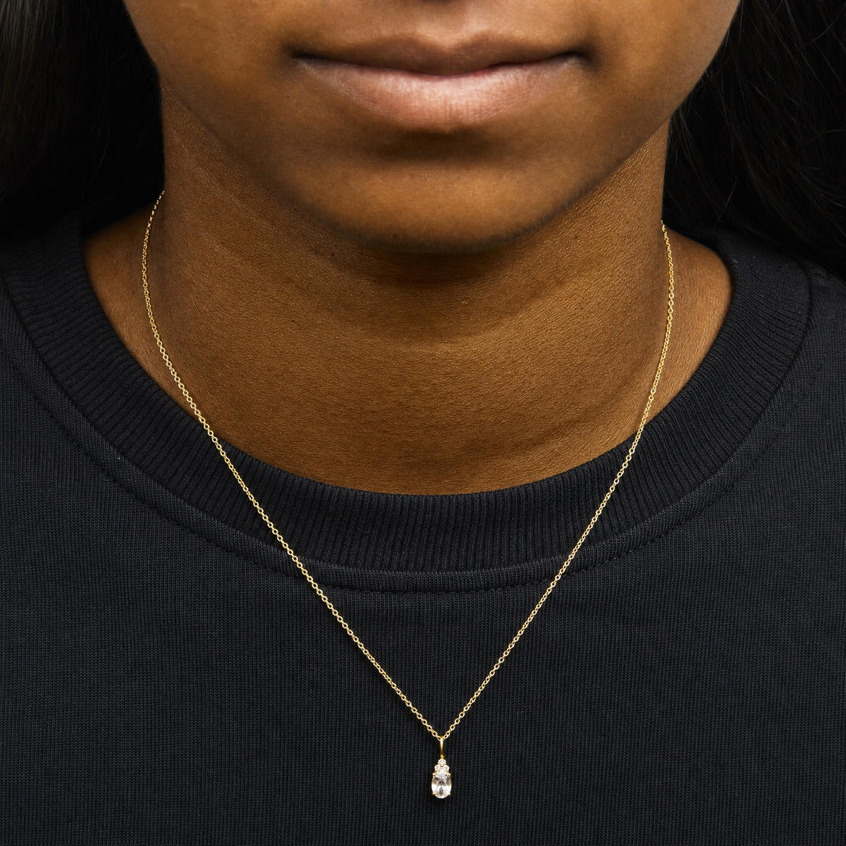 Close-up front view of a model wearing a yellow metal necklace with a pendant featuring one oval white gemstone and three small round white gemstones in prong settings.