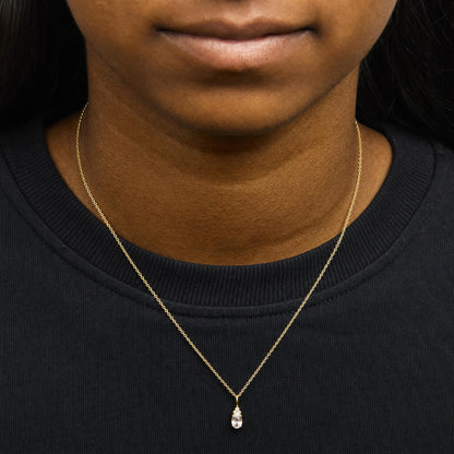 Close-up front view of a model wearing a yellow metal necklace with a pendant featuring one oval white gemstone and three small round white gemstones in prong settings.