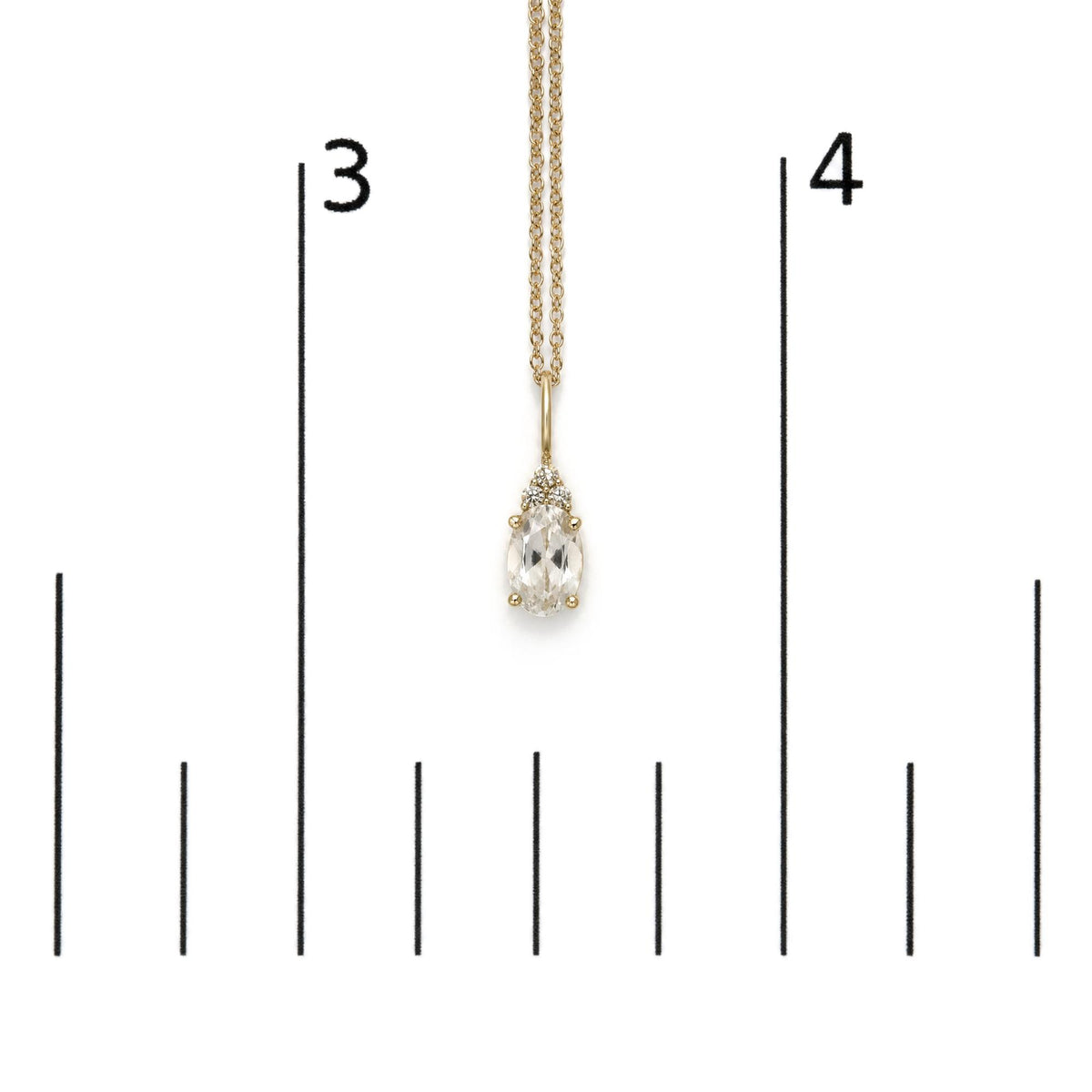 Yellow metal necklace with an oval white gemstone pendant surrounded by three round white gemstones in prong settings, shown on a scale, front angle.