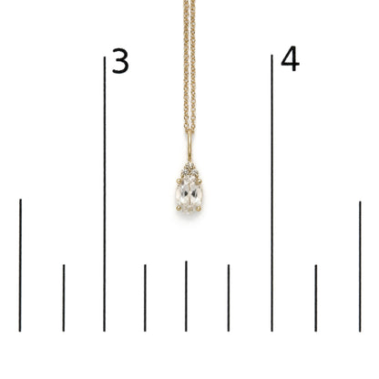 Yellow metal necklace with an oval white gemstone pendant surrounded by three round white gemstones in prong settings, shown on a scale, front angle.