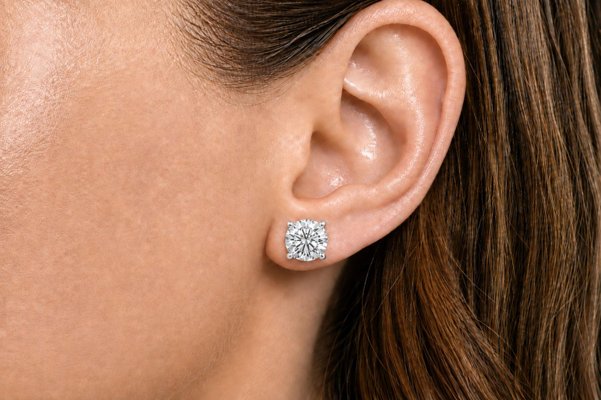 Close-up side view of a model wearing a white metal stud earring with a round white gemstone in a 4-prong setting.