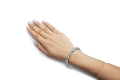 Close-up angled view of a white metal bracelet with round white gemstones in prong settings, worn on a model's wrist.
