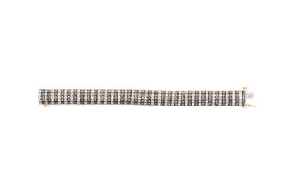 Close-up shot of a yellow metal bracelet laid flat, featuring alternating rows of round brown and white gemstones in prong settings.