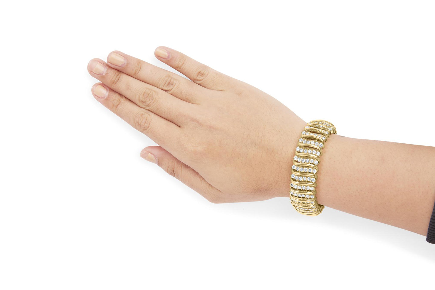 Yellow metal bracelet with curved rows of white round gemstones in prong settings, shown on a model hand from a top angle.