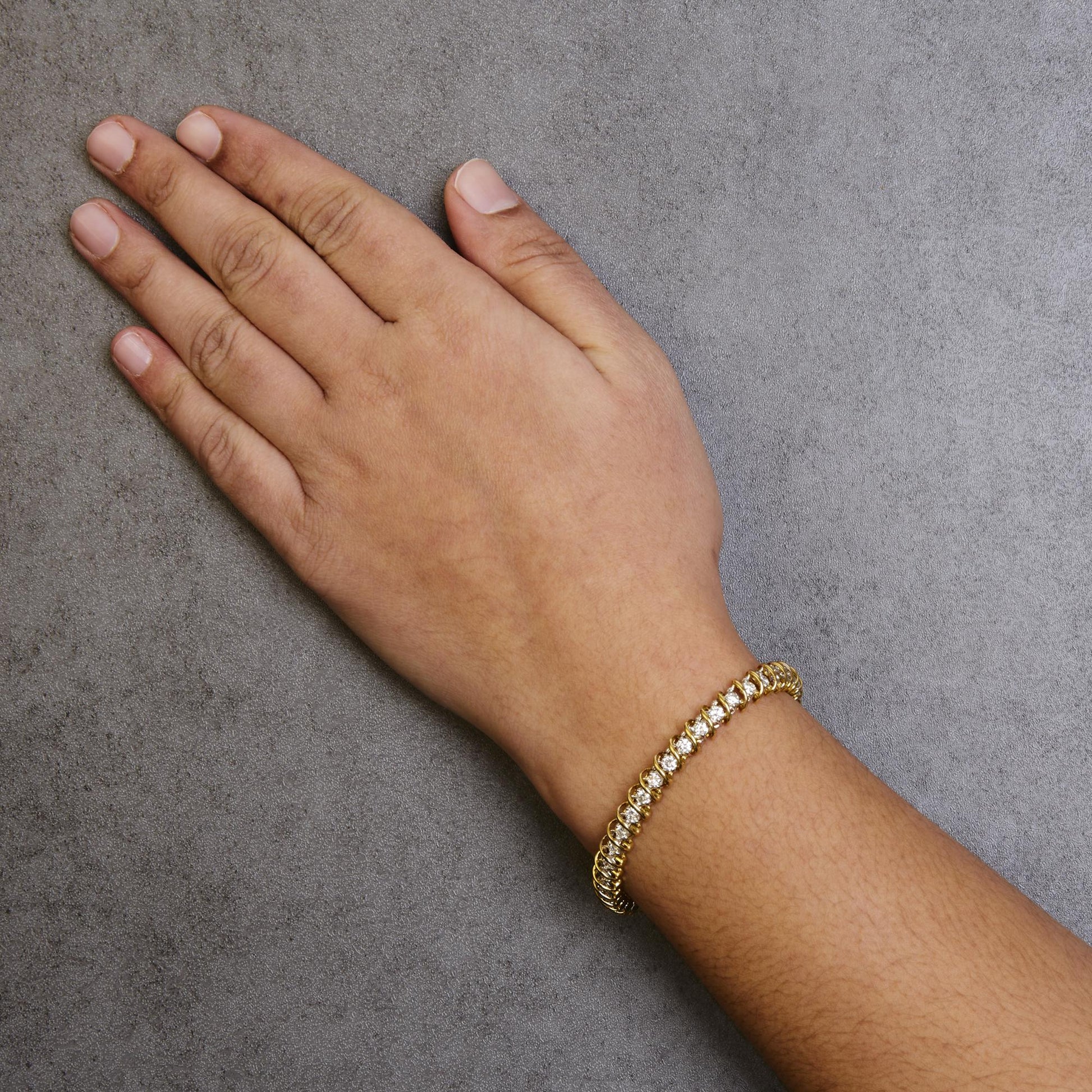 Close-up angled shot of a yellow metal bracelet with round white gemstones in 2-prong settings, worn on a model's wrist.