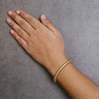Close-up angled shot of a yellow metal bracelet with round white gemstones in 2-prong settings, worn on a model's wrist.