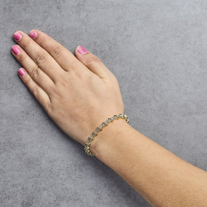Yellow metal bracelet with round white gemstones in prong settings, shown worn on a model's wrist from a top-side angle.