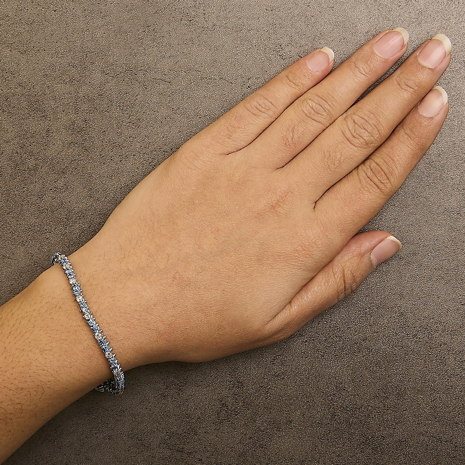 White metal bracelet with alternating white and blue round gemstones in 3-prong settings, shown worn on a model's wrist from a top angle.