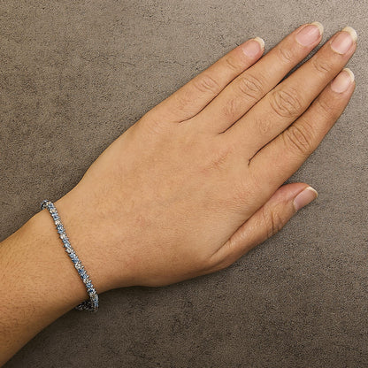 White metal bracelet with alternating white and blue round gemstones in 3-prong settings, shown worn on a model's wrist from a top angle.