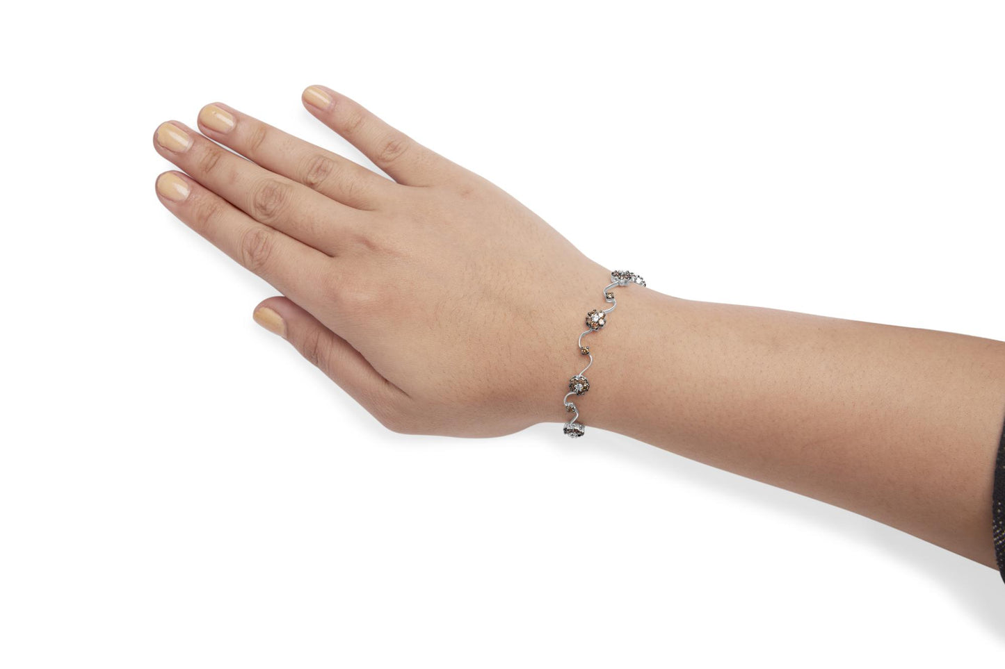 White metal bracelet with alternating clusters of white and champagne round gemstones in prong settings, shown on a model's wrist with hand extended, angled from above.