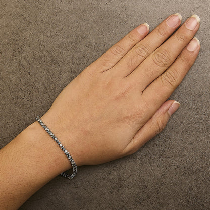 Top view of a wrist wearing a white metal bracelet featuring round white and blue gemstones in prong settings.